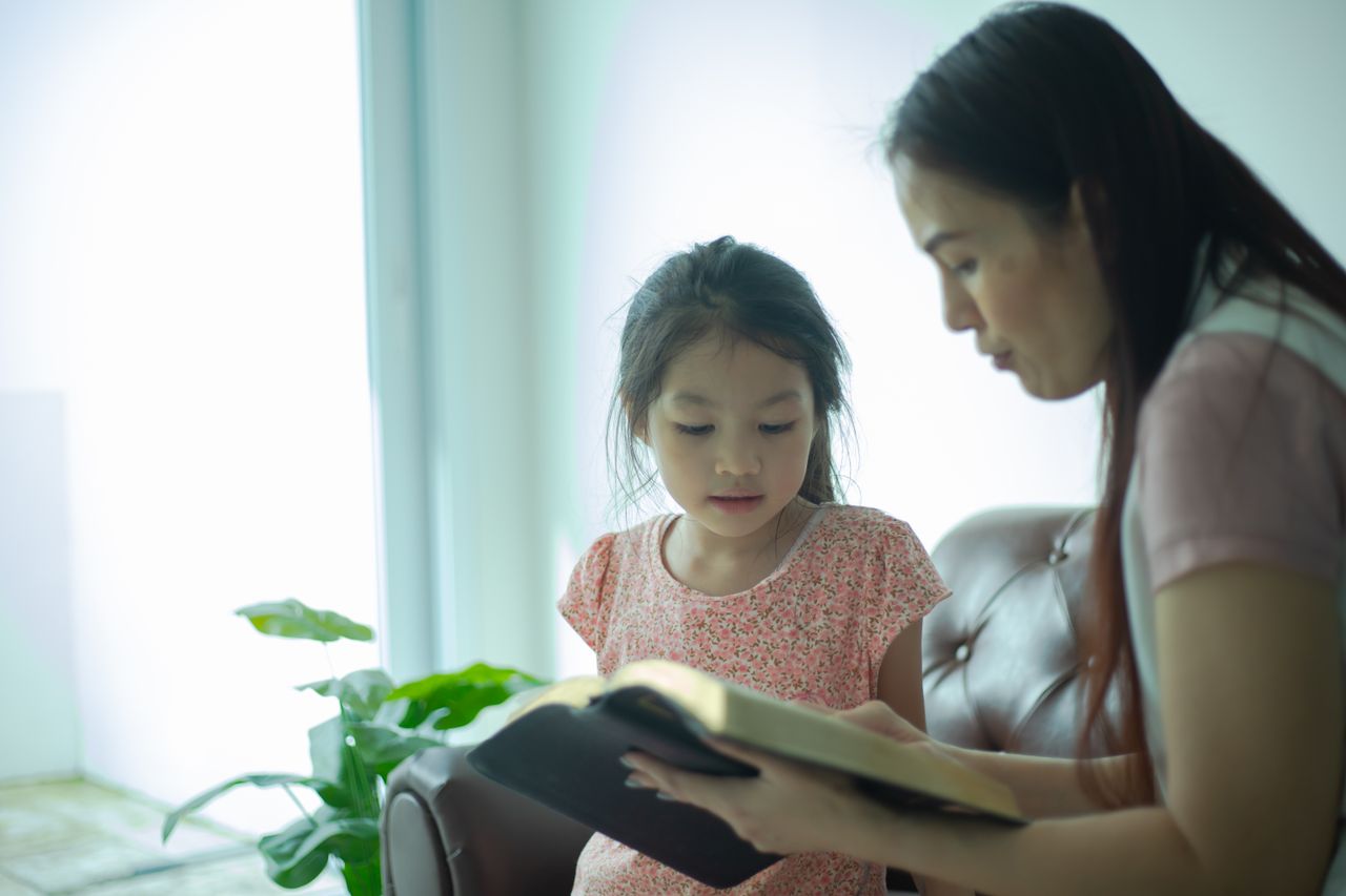 A mother and daughter share a bonding moment reading a book indoors.