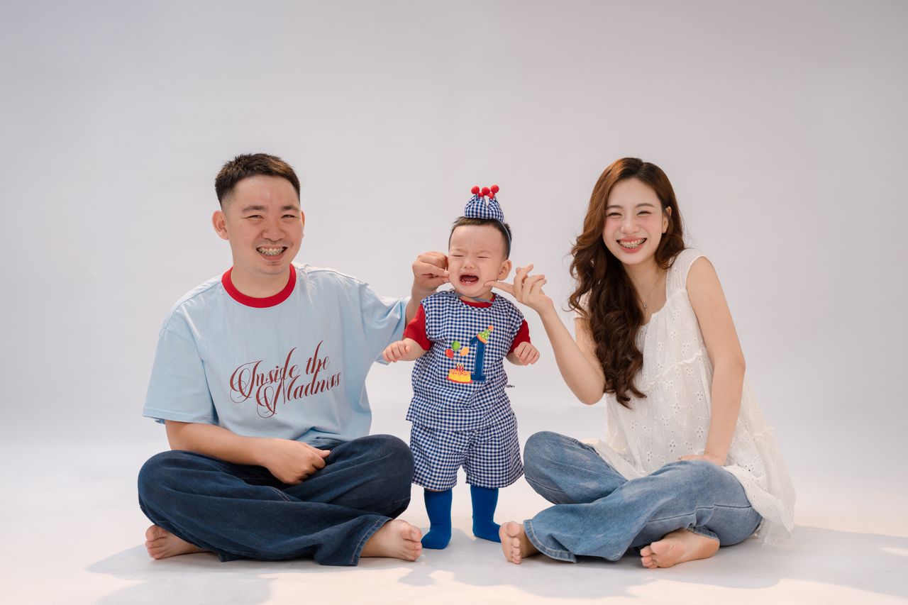 Cheerful parents with their crying baby during a family photo session in a studio setting.