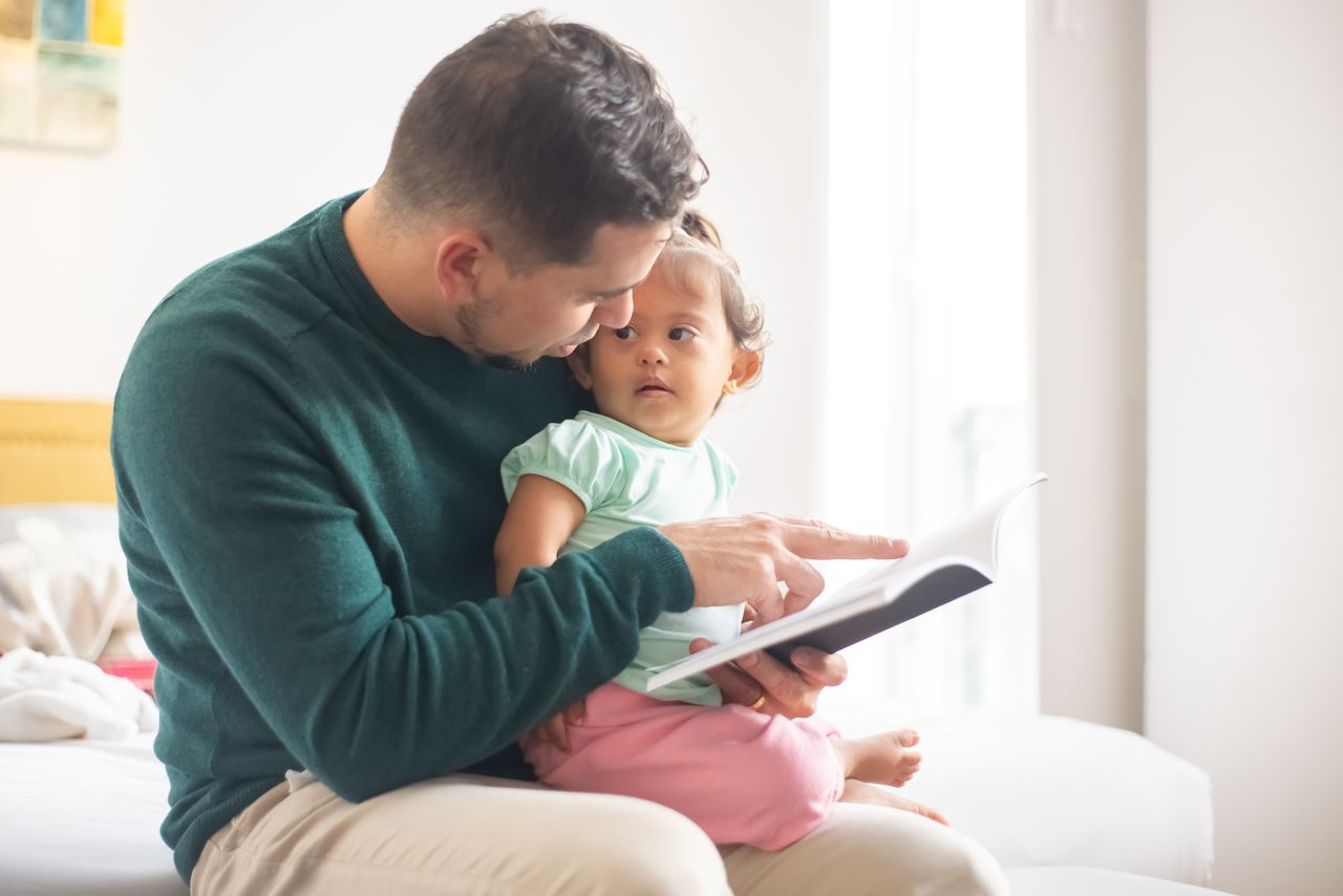 A tender moment as a father reads a book to his young daughter at home.